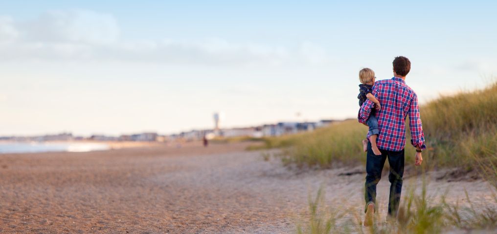 Photograph of father holding a young child on the beach.